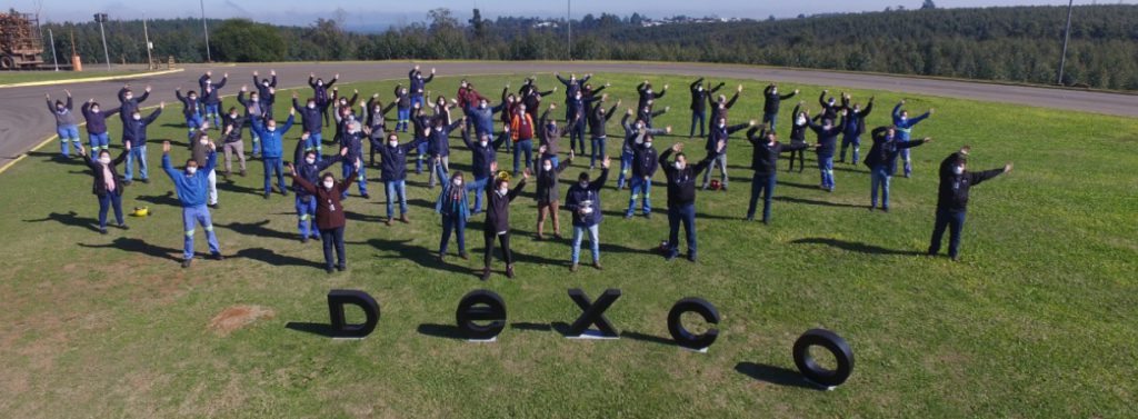 Grupo de profissionais uniformizados de azul e reunidos em um campo, com letras formando a palavra Dexco à frente