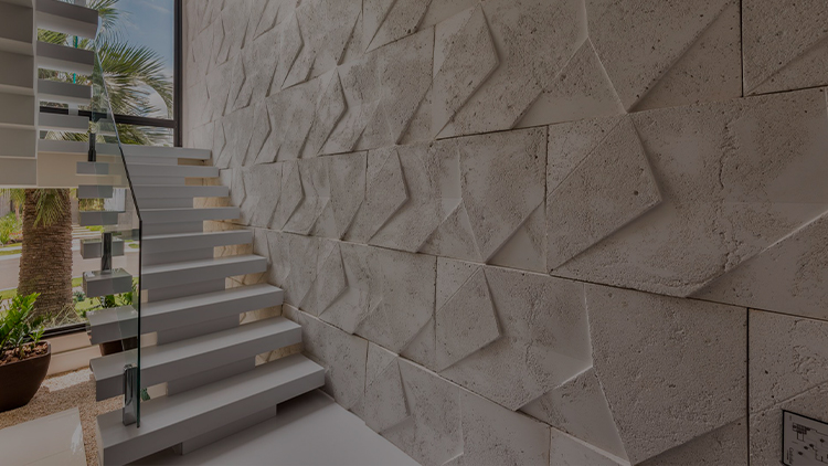 Ambiente iluminado de uma casa, com uma escada branca em primeiro plano e, ao lado dela, uma parede com textura formando triângulos da Castelatto.